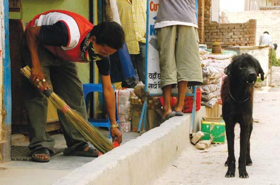 (above) A Boudhanath area shopkeeper sweeps the dusty sidewalk, as a street dog stands nearby. (facing page) A pair of street dogs lounge in the shade under a table on a restaurant s patio.