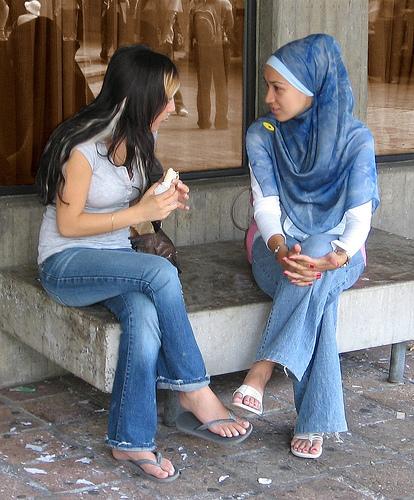 Two girls take a break to sit and talk. Two women are sitting, and one of them is holding something.